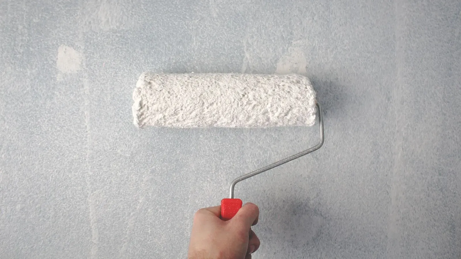A paint roller applying fresh white paint to a wall